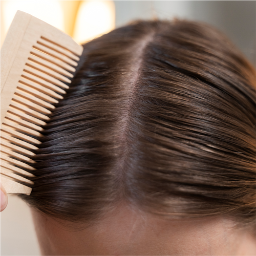 Close-up view of healthy dark brown hair parted in the middle with a wooden comb styling smooth hair strands.