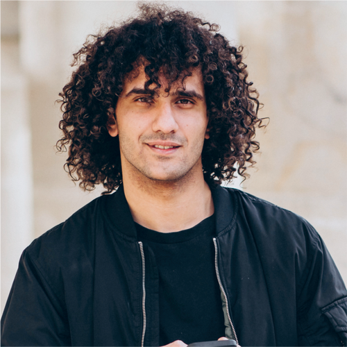 Young man with naturally curly, voluminous dark hair smiling at the camera.